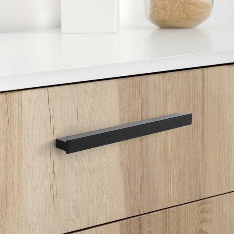 Close-up of a black linear cabinet handle on a light wooden cabinet door